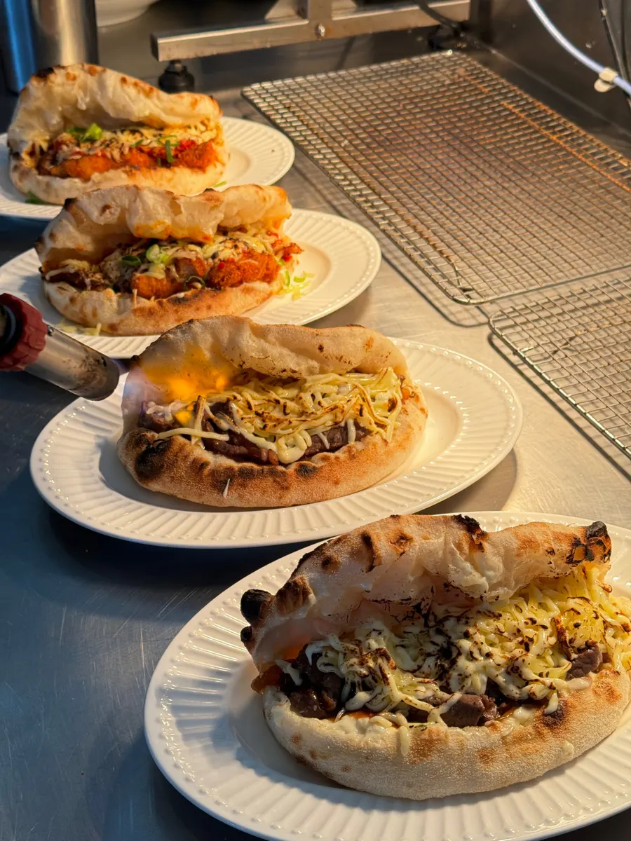 Three pizza sandwiches on plates at the pass, folded woodfired dough with melted fillings