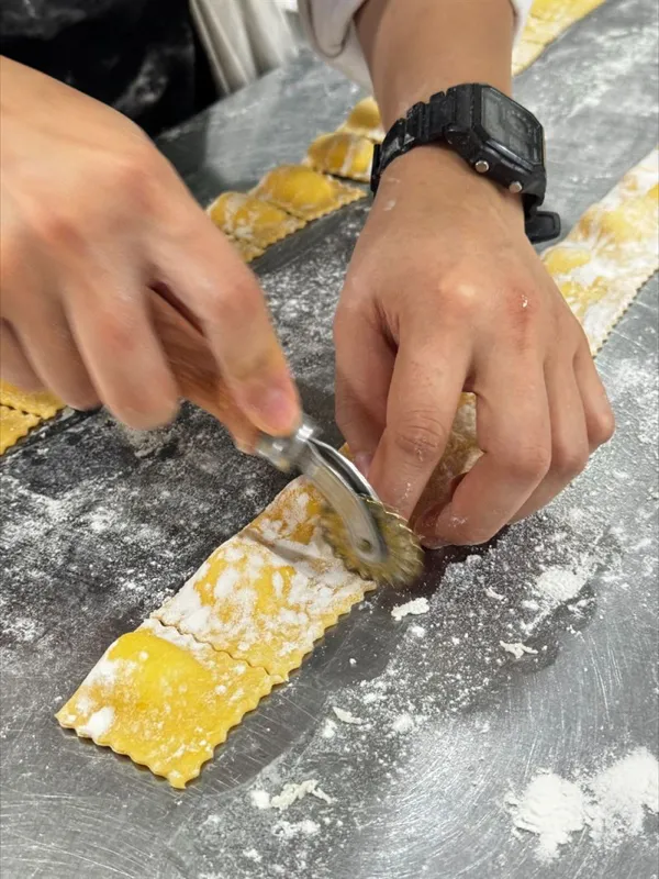 Hands cutting a strip of filled ravioli on a floured bench
